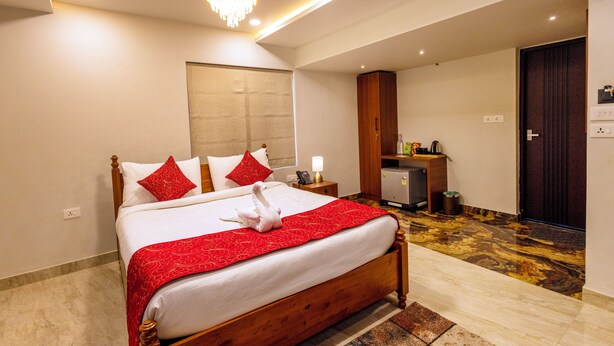 A hotel room with a large bed, a chandelier, a desk, and a minibar. - Chechus Beach Walk (Varkala)