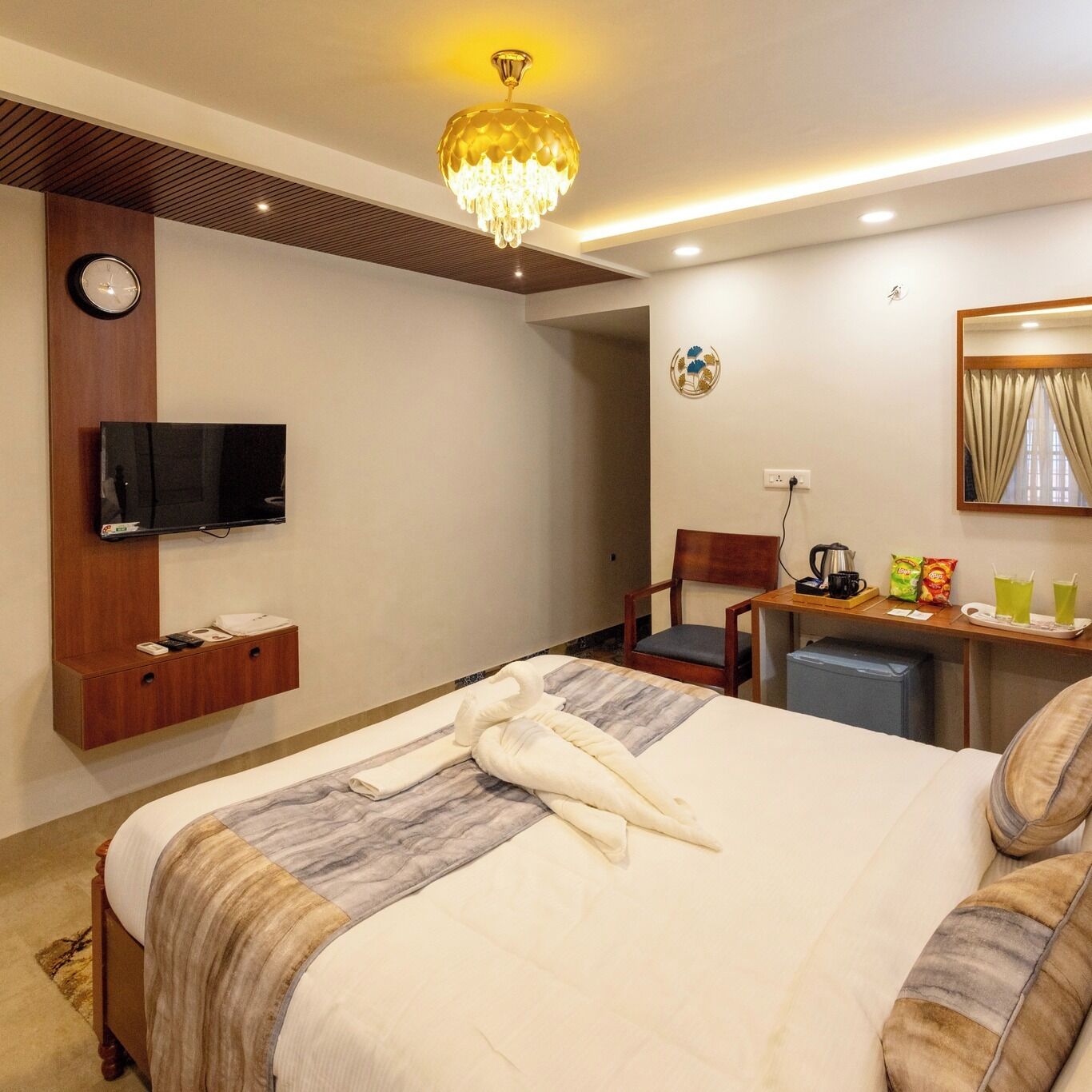 Habitación de hotel con cama, televisor, escritorio con silla, cafetera y espejo.