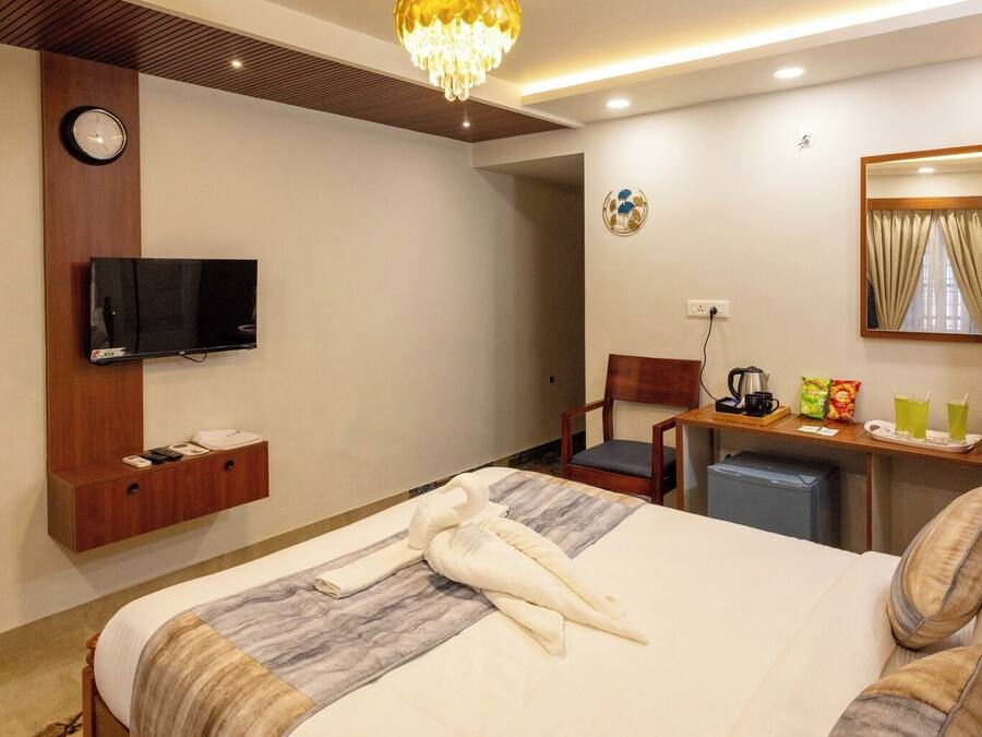 Habitación de hotel con cama, televisor, escritorio con silla, cafetera y espejo.