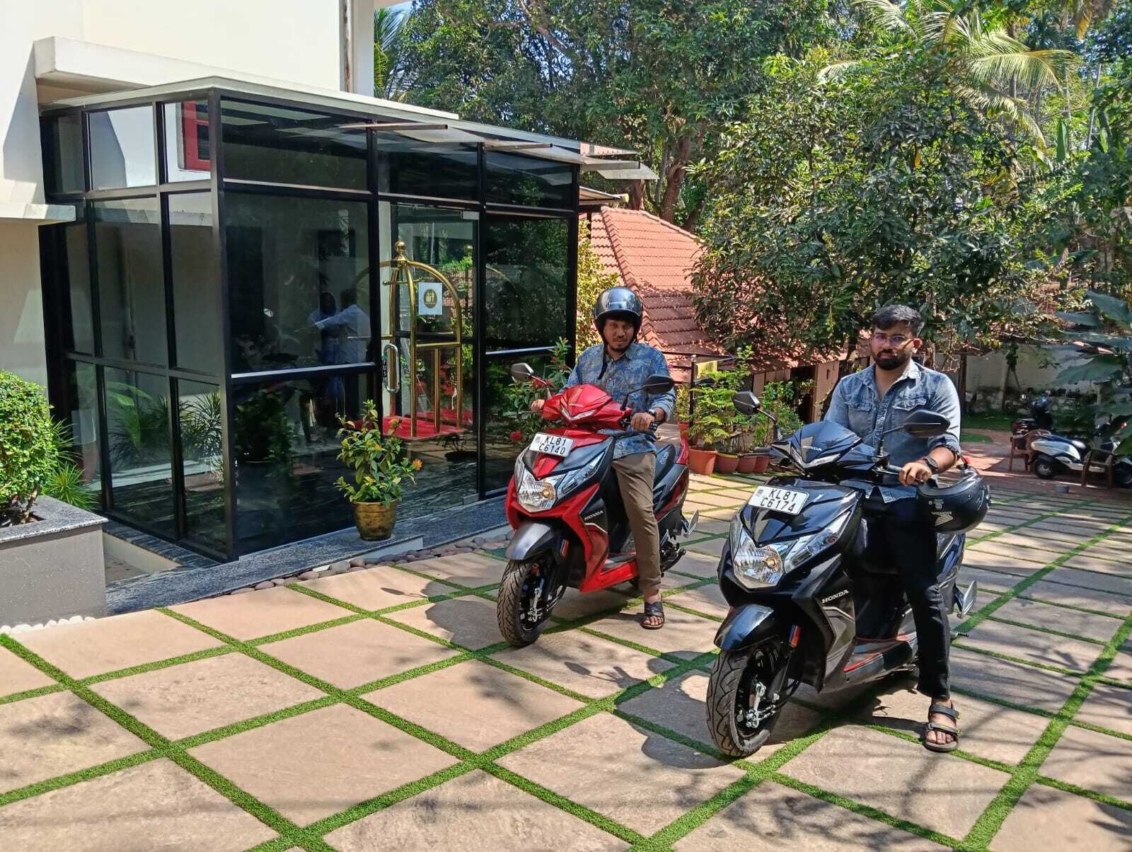 Dos motocicletas estacionadas frente a un edificio con acceso de vidrio y un patio con baldosas.