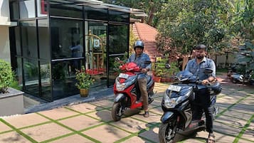 Dos motocicletas estacionadas frente a un edificio con acceso de vidrio y un patio con baldosas.