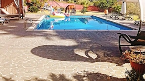 Une piscine dotée de chaises longues et d’un espace abrité, entourée d’une terrasse en pierre et de verdure.
