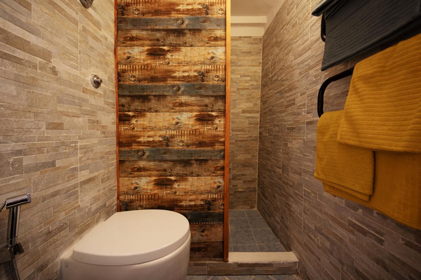 Ein Badezimmer mit einer Wand in Holzoptik, einer weißen Toilette und einem gelben Handtuch an einem Handtuchhalter.