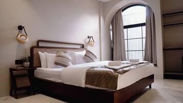 A neatly made bed with a wooden headboard, a bedside table with a lamp, and a large arched window with curtains.