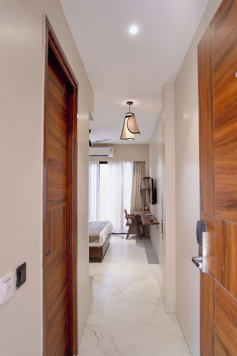 A hotel room with a wooden door, a bed, a desk, and a hanging light fixture.