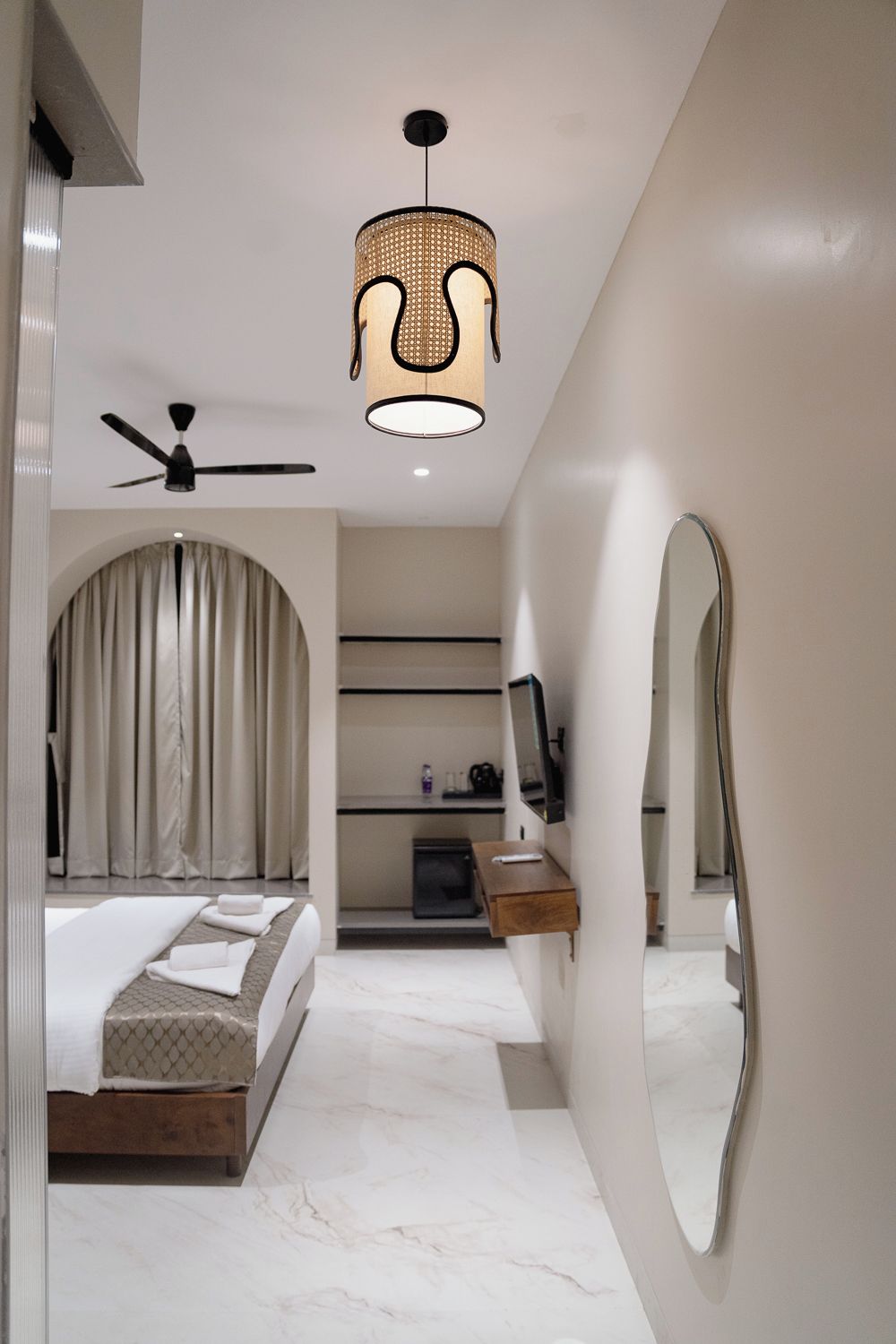 A modern bedroom with a bed, a ceiling fan, a large mirror, and a pendant light.