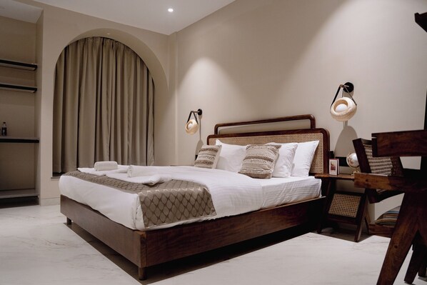 Une chambre à coucher bien aménagée, avec un grand lit, une tête de lit en bois et deux lampes fixées au mur.