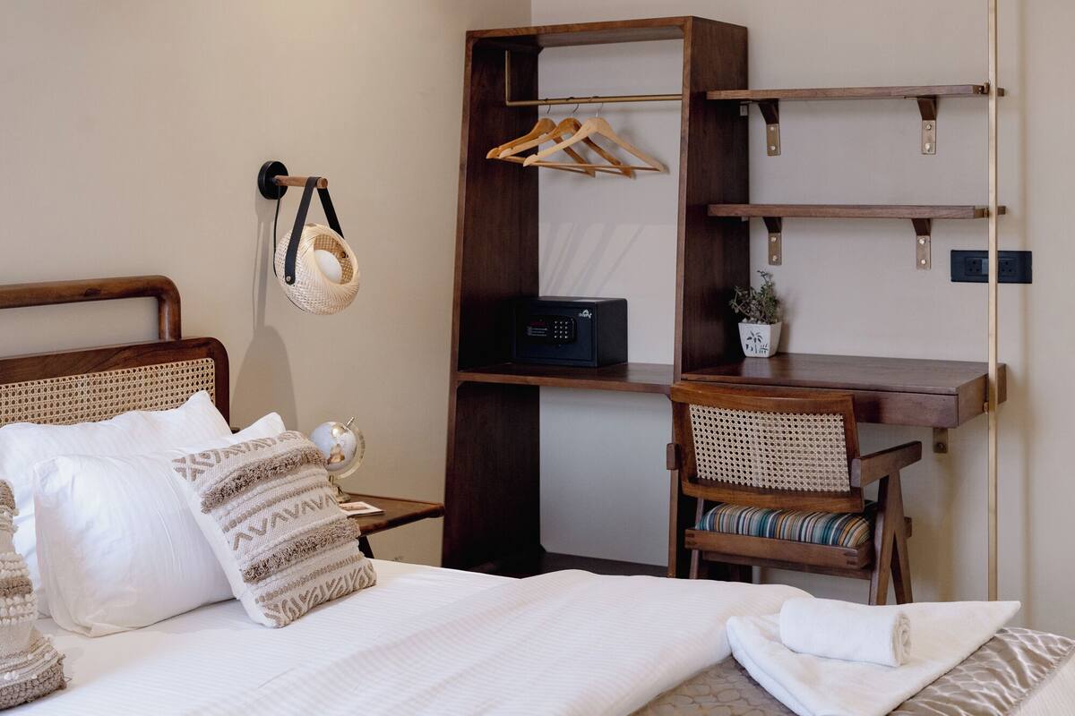 A neatly arranged bedroom with a bed, a bedside table, a chair, a desk with shelves, and a hanging basket.