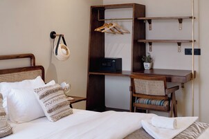A neatly arranged bedroom with a bed, a bedside table, a chair, a desk with shelves, and a hanging basket.