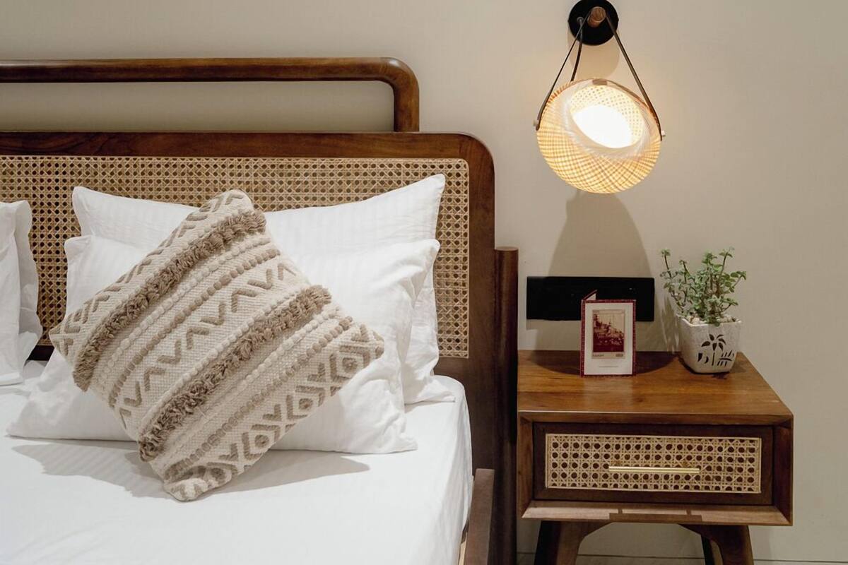 A neatly made bed with a patterned pillow and a bedside lamp on a wooden nightstand.