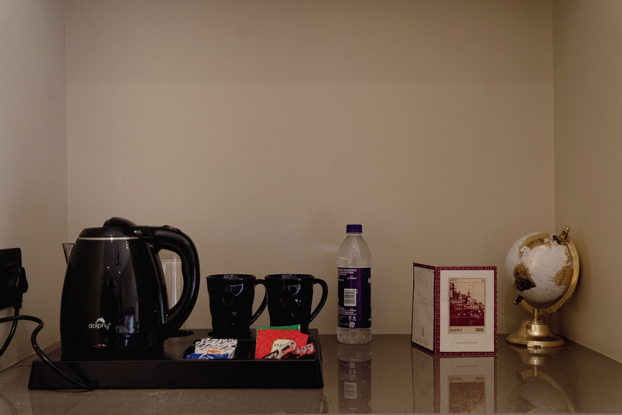 A coffee station with a coffee maker, two cups, a bottle of water, a box of tissues, and a globe.