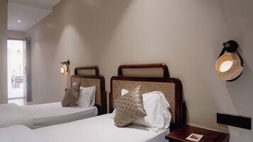 Habitación de hotel con dos camas individuales, una mesita de noche pequeña con un libro, una lámpara de pared y vistas al exterior.
