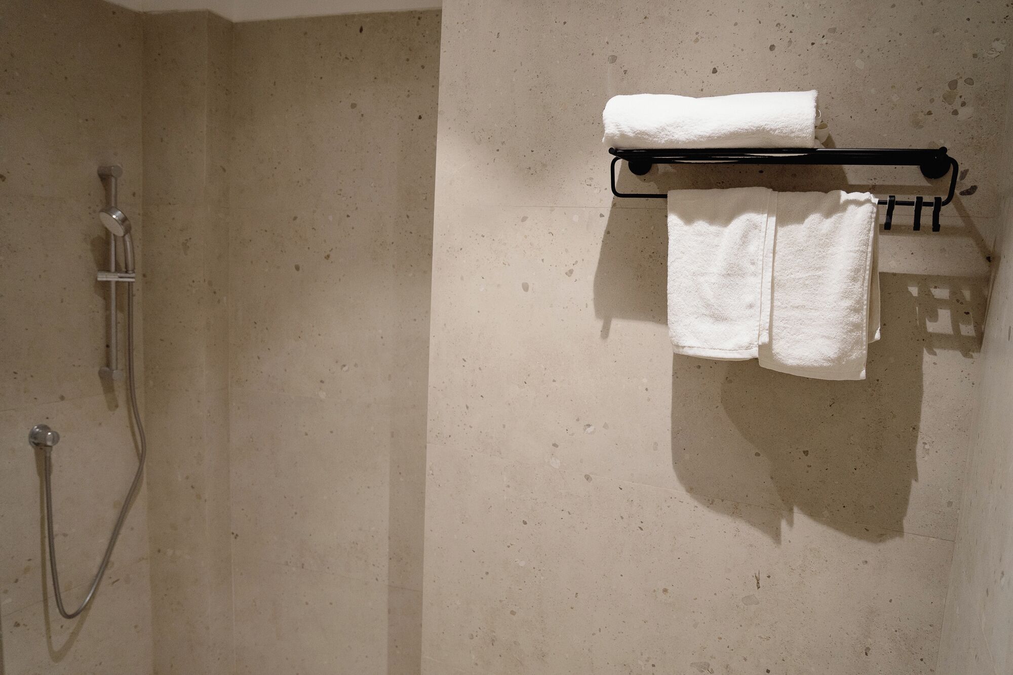 A bathroom with a shower, a towel rack with two towels, and a wall-mounted towel warmer.