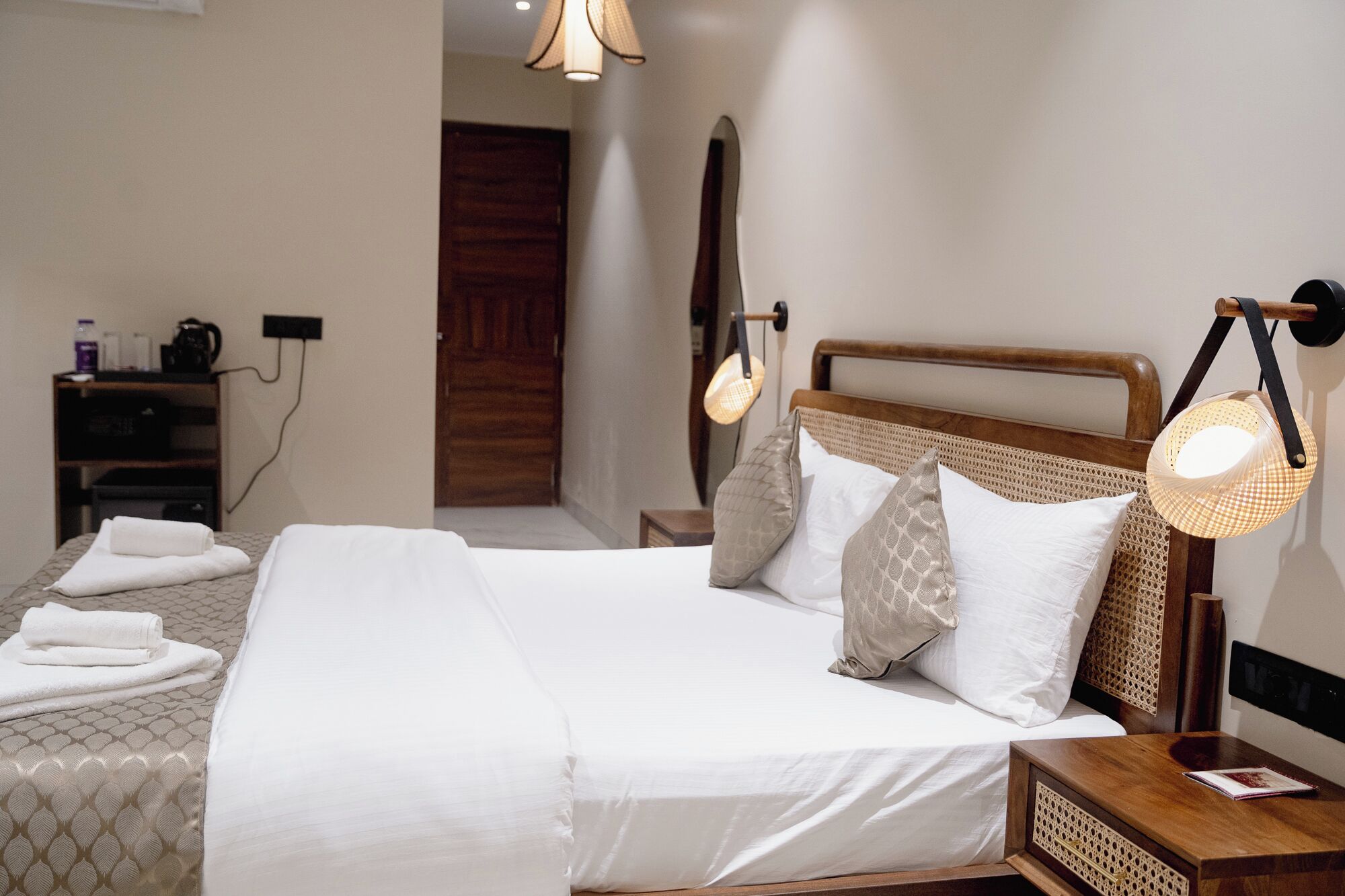 A neatly made bed with white linens and a wooden headboard, a bedside table with a lamp, and a small wooden nightstand.