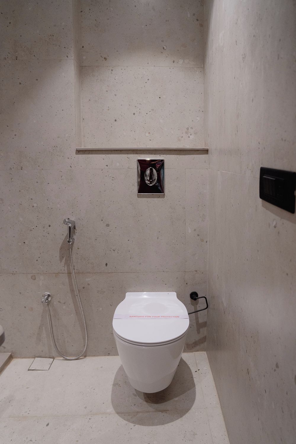 Un baño moderno con inodoro blanco, ducha de mano y un sistema de descarga empotrado.