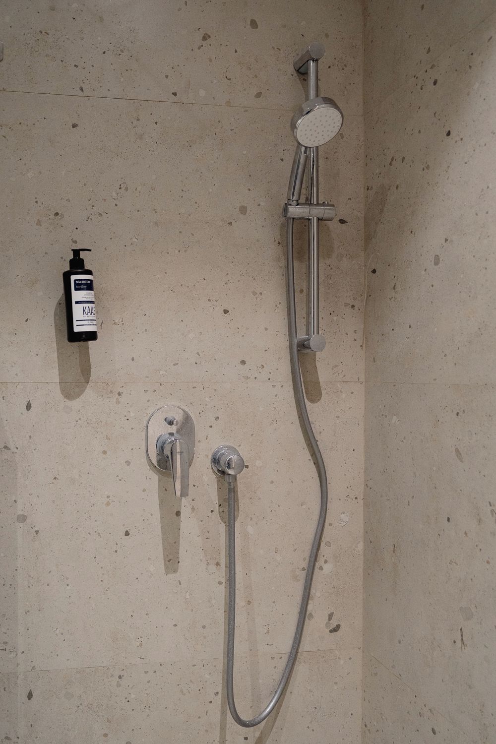 A shower with a handheld showerhead and a wall-mounted faucet.