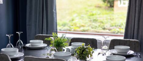 Mesa de comedor preparada para seis personas, con platos, tazones y cubiertos blancos, y sillas a cada lado.
