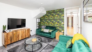 Una sala de estar moderna con un televisor de pantalla plana grande, un mueble de madera, un sofá verde y un papel tapiz estampado.