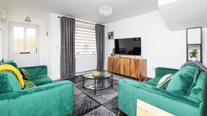 Una sala de estar moderna con sofás verdes, una mesa de centro de vidrio, un mueble de madera y un televisor de pantalla plana.