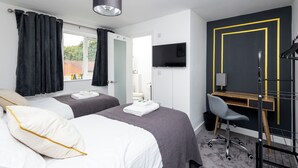 Habitación de hotel con dos camas, un escritorio, una silla, un televisor y una ventana con cortinas.
