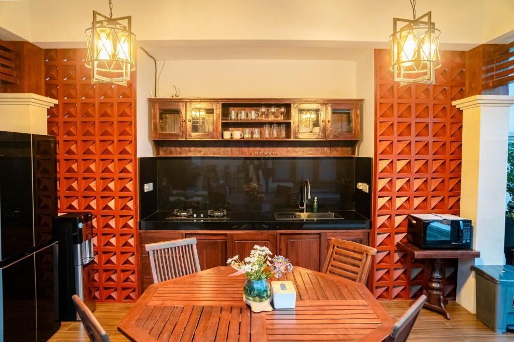 A kitchen with wooden cabinets, a black countertop, and a dining table with chairs. There is a microwave on a small table next to the kitchen.