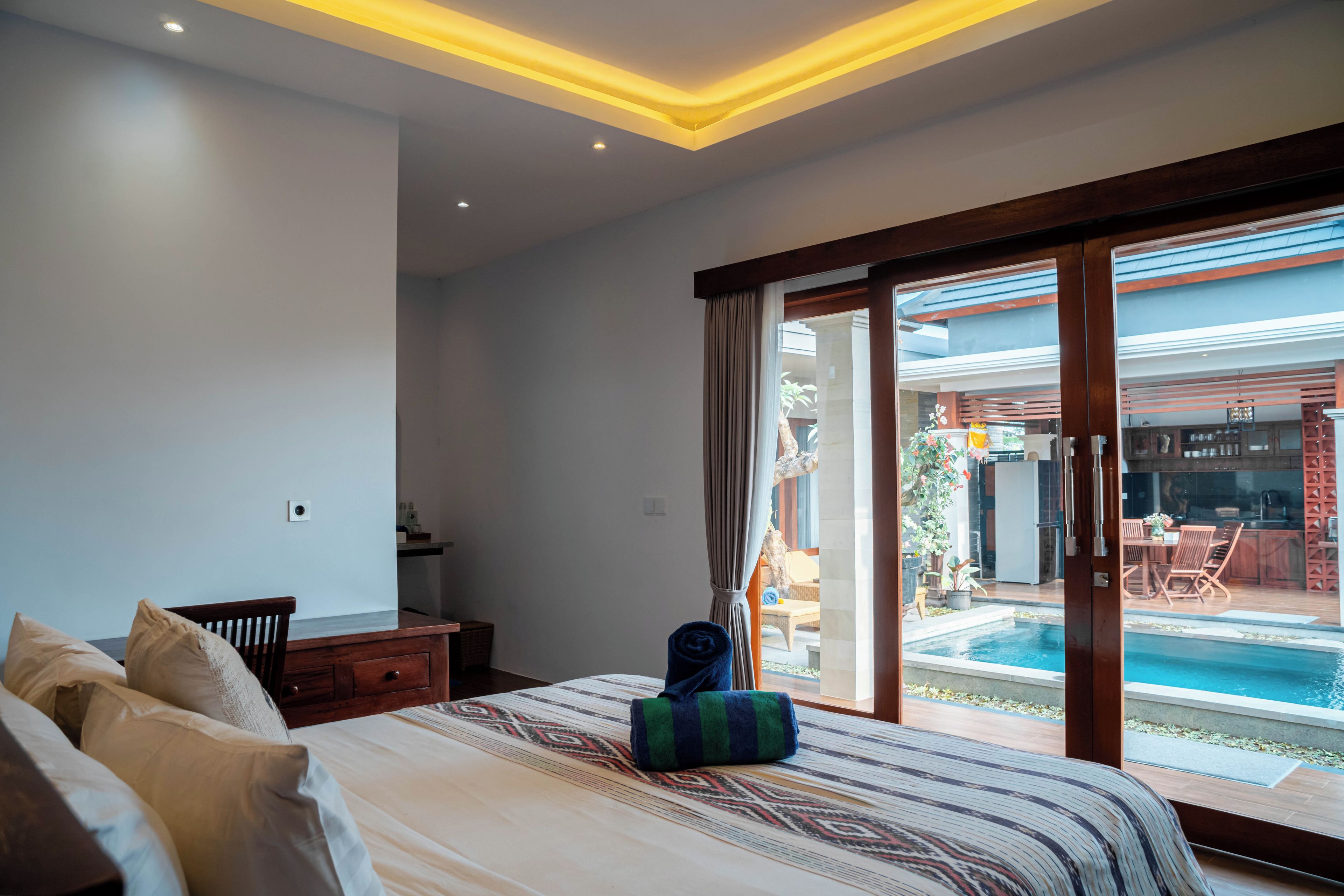 A bedroom with a large bed, a nightstand, and a view of an outdoor swimming pool through a sliding glass door.