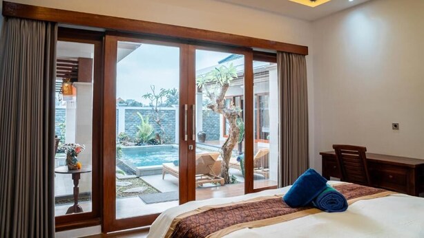 A hotel room with a bed, a desk, and a view of a swimming pool and garden. - Darta Ubud Rice Field Villas by EPS (Ubud)
