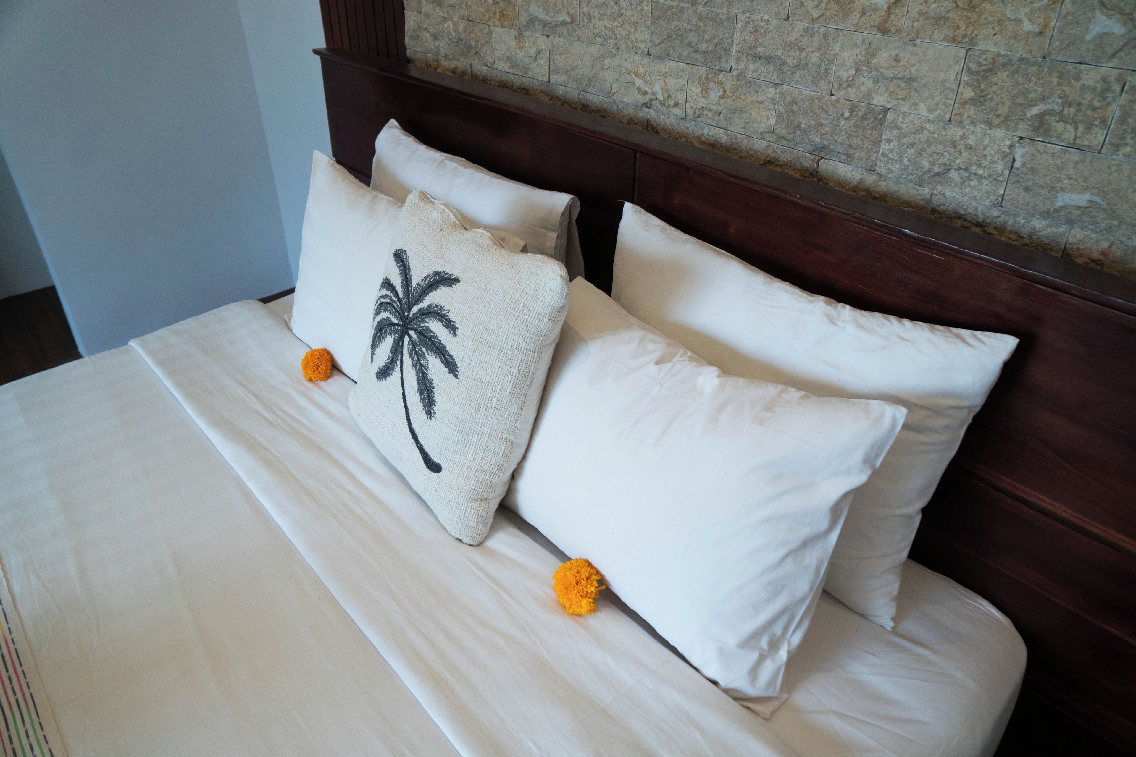A bed with white linens and two pillows, one with a palm tree design.