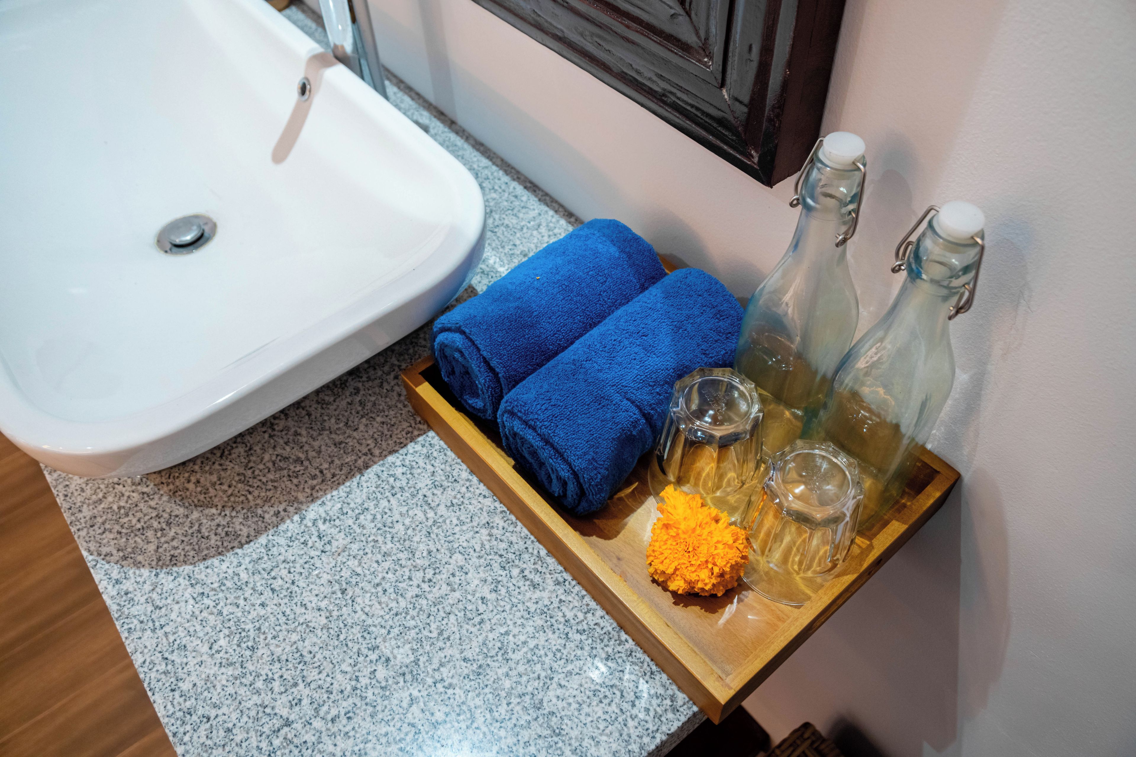 Un lavabo, un vassoio di legno con un asciugamano blu, due bottiglie di vetro e una spugna.