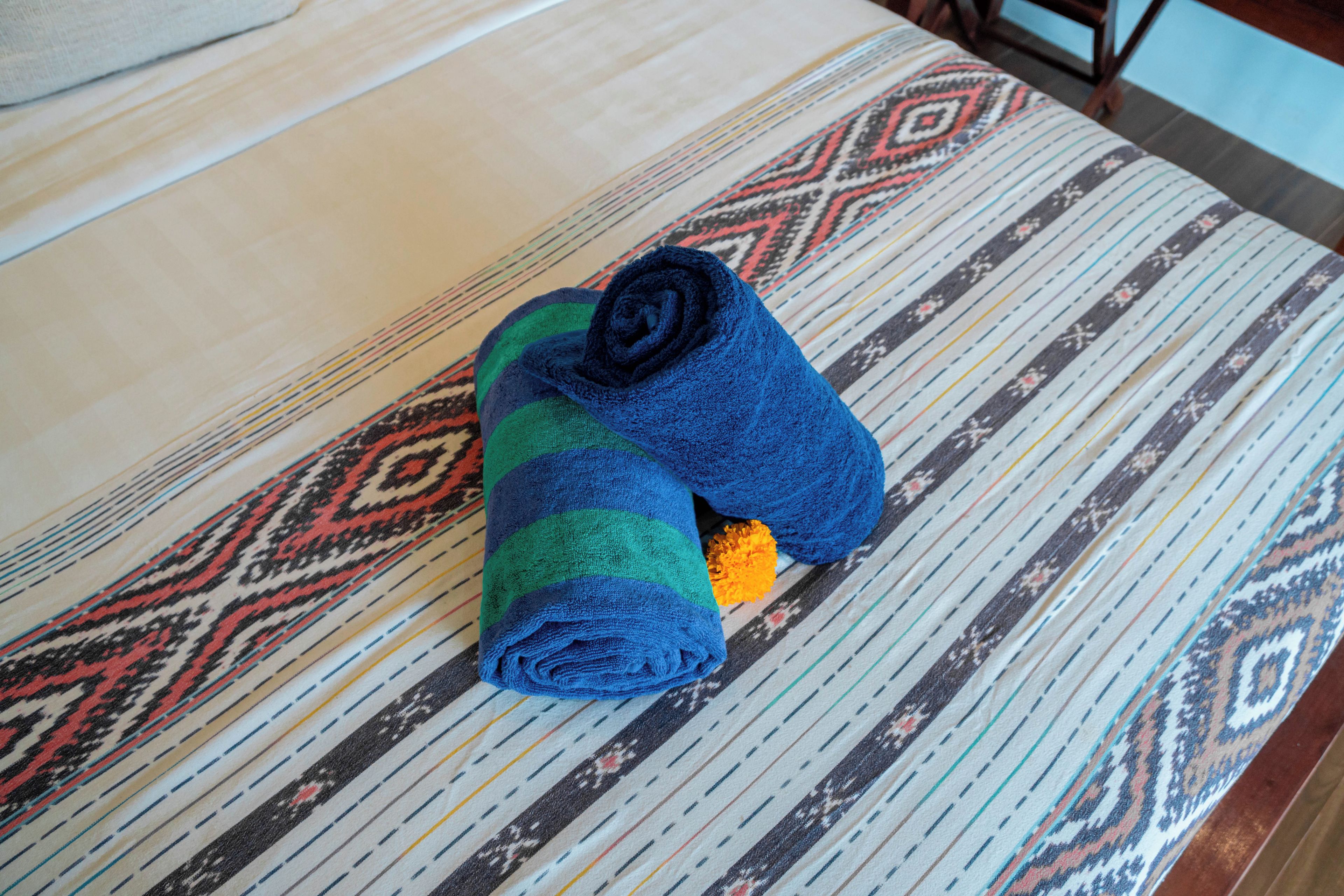 A bed with a patterned bedspread and a rolled-up towel with a blue and green stripe pattern.
