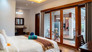 A hotel room with a bed, a bathroom, and a sliding glass door leading to an outdoor area.
