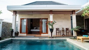 A modern house with a swimming pool, a patio with chairs, and a bed visible through the open door. - Darta Ubud Rice Field Villas by EPS (Ubud)