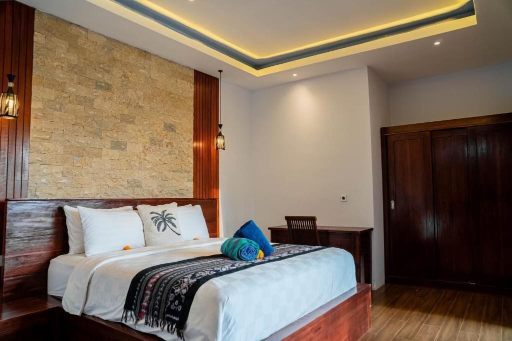 A modern hotel room with a stone accent wall, a wooden bed frame, and a desk with a chair.