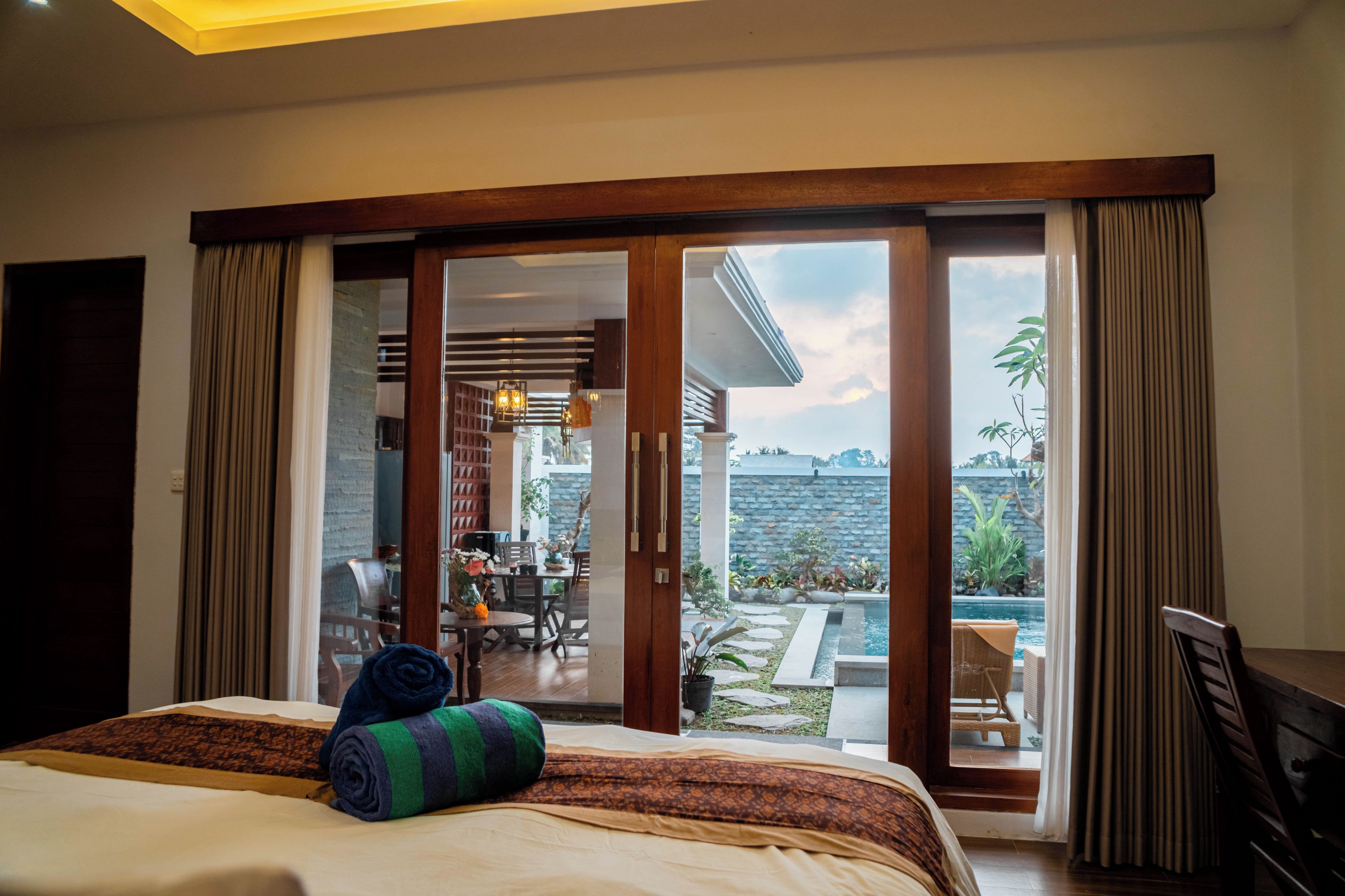 Quarto de hotel com cama e vista para a área externa, incluindo piscina e espaço para refeições.