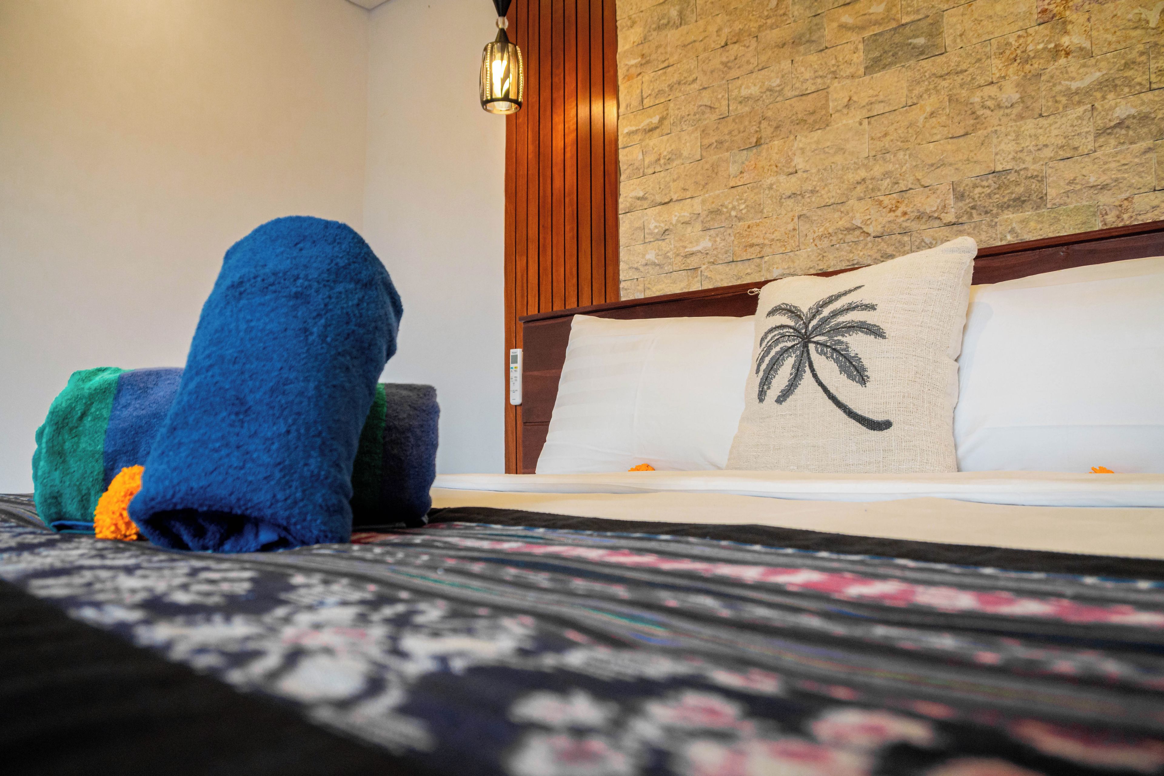 A hotel room with a bed, a wooden headboard, a stone wall, and a hanging light fixture.