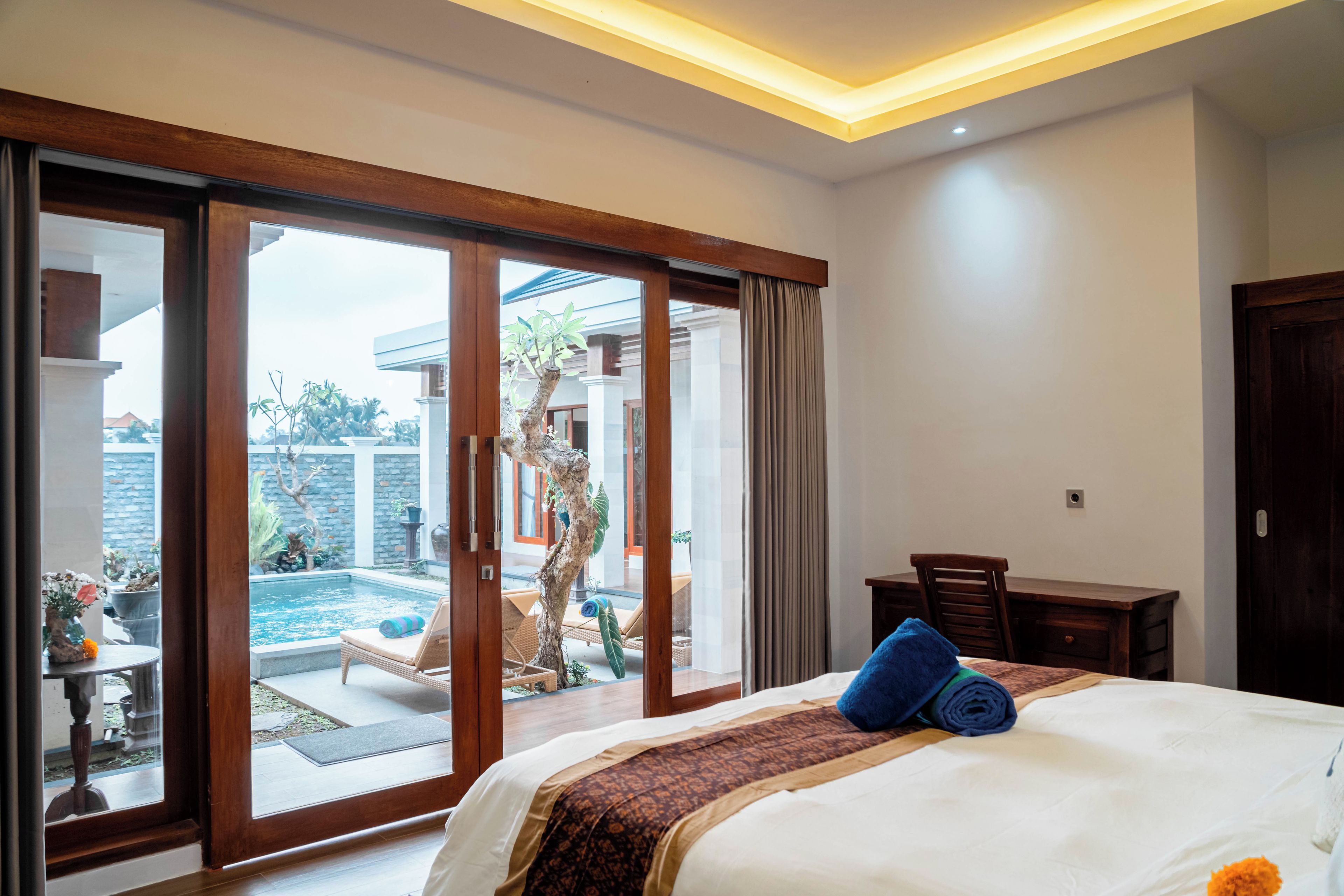 Una habitación de hotel con cama, escritorio y vistas a la piscina exterior.