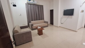 A modern living room with a sofa, a small table, a TV mounted on the wall, and a door leading to another room. - STAR 4 SEASON (Salalah)