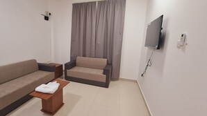 A modern living room with two sofas, a small wooden table, a TV mounted on the wall, and a curtain. - STAR 4 SEASON (Salalah)