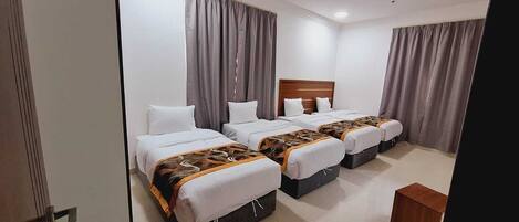 Ein Hotelzimmer mit drei Betten, grauen Vorhängen und einem Holzkopfende.