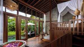 A spacious room with a large window, a wooden floor, a white bed, and a small table. - The Pulu Villas by GenuineHost (Ubud)