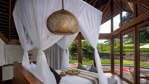 A bedroom with a canopy bed, a wooden bench, and a view of a garden through large windows. - The Pulu Villas by GenuineHost (Ubud)