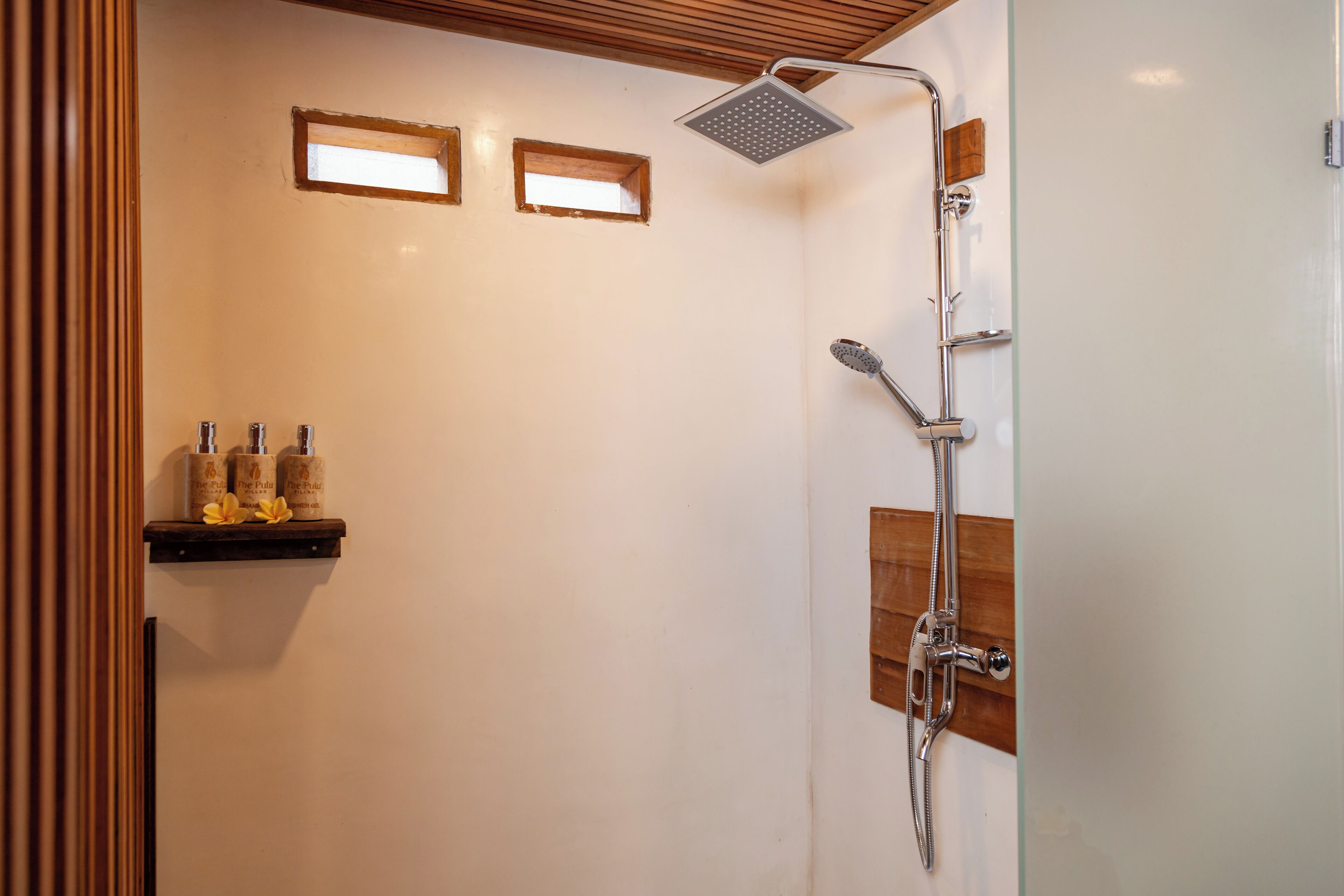 A shower with a handheld showerhead and a wall-mounted rain showerhead. There are two small windows on the wall above the shower.