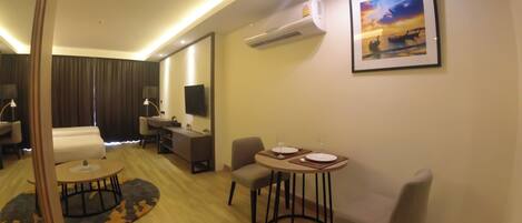 A hotel room with a bed, a desk, a chair, a dining table with plates and glasses, a TV, and an air conditioner.