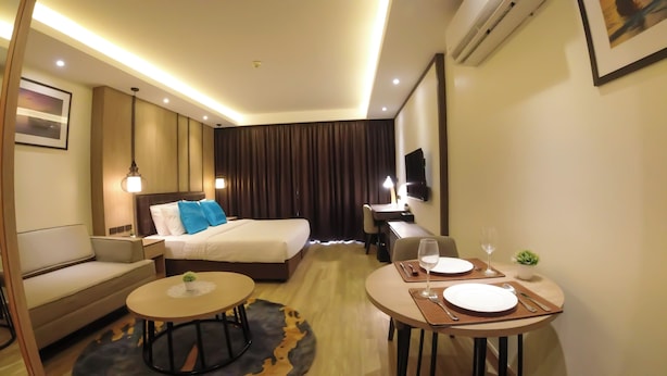 A hotel room with a bed, a sofa, a desk with a chair, a dining table with plates and cutlery, and a small plant. - Wyatt Hotel Jomtien Beach (Pattaya)