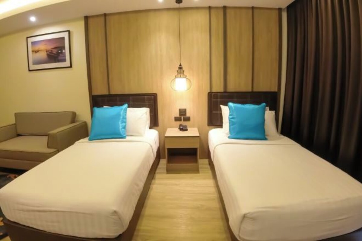 Habitación de hotel con dos camas, una mesita de noche, una lámpara, una silla y un cuadro en la pared.