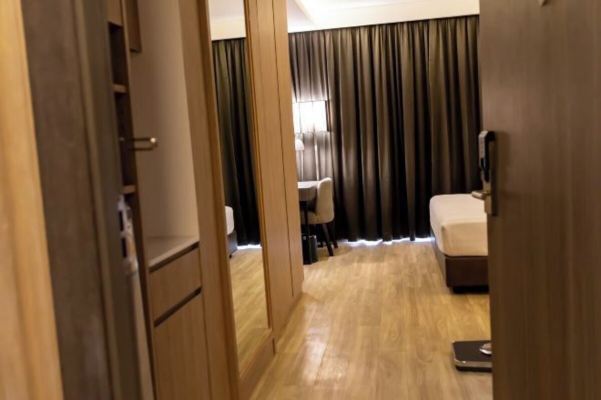 Una habitación de hotel con suelo de madera, una cama, un escritorio con una silla y una ventana con cortinas.