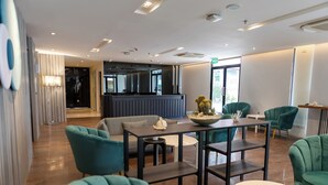 A modern hotel lobby with teal armchairs, a central table with a bowl, and a seating area with a sofa and a small table. - Wyatt Hotel Jomtien Beach (Pattaya)