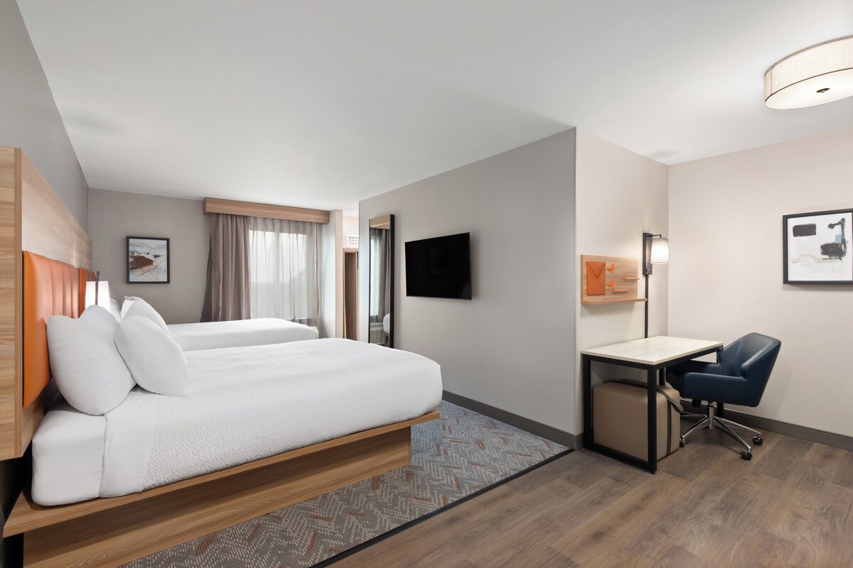A hotel room with a bed, a desk, a chair, a TV, and a window with curtains.