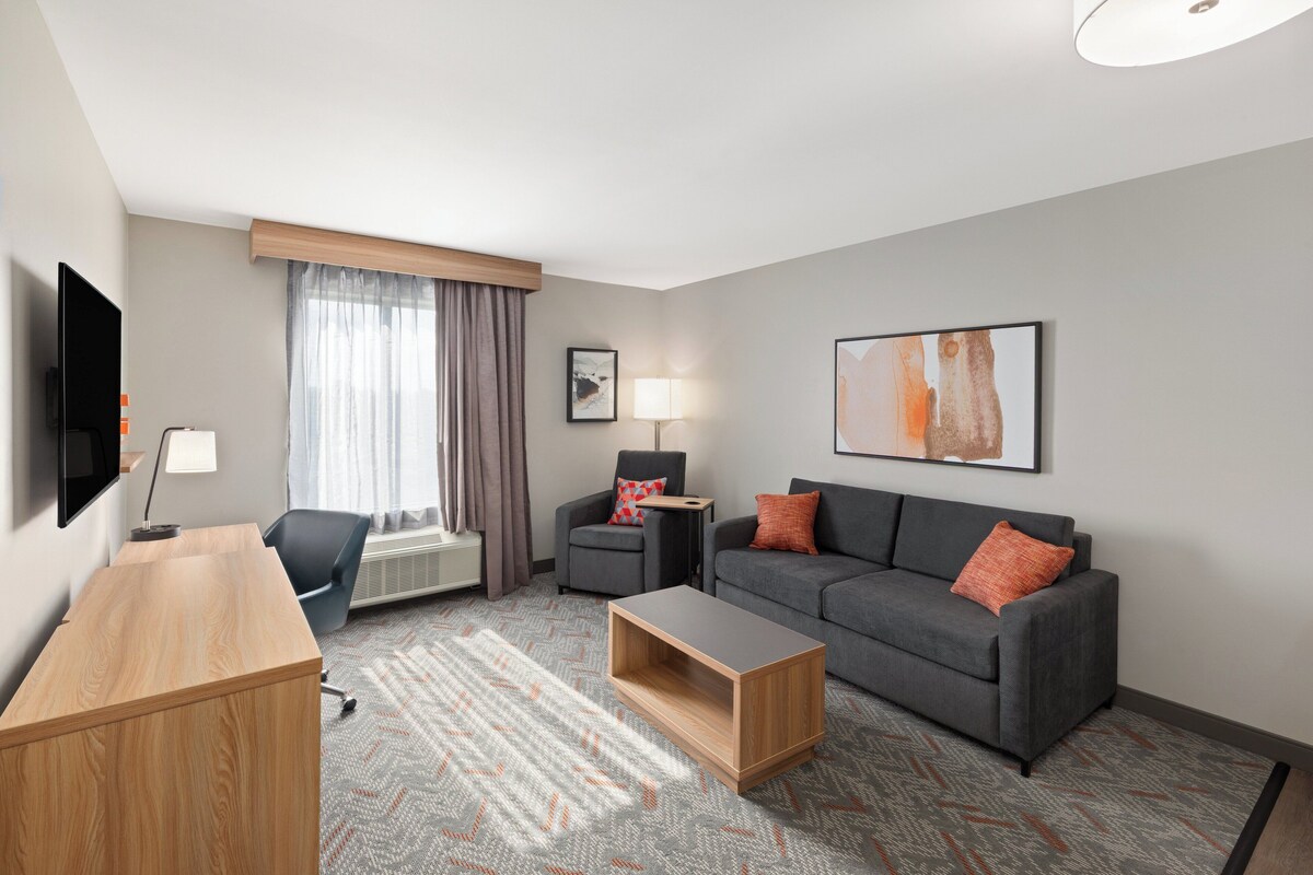 A modern hotel room with a wooden desk, grey sofa, and a flat-screen TV.