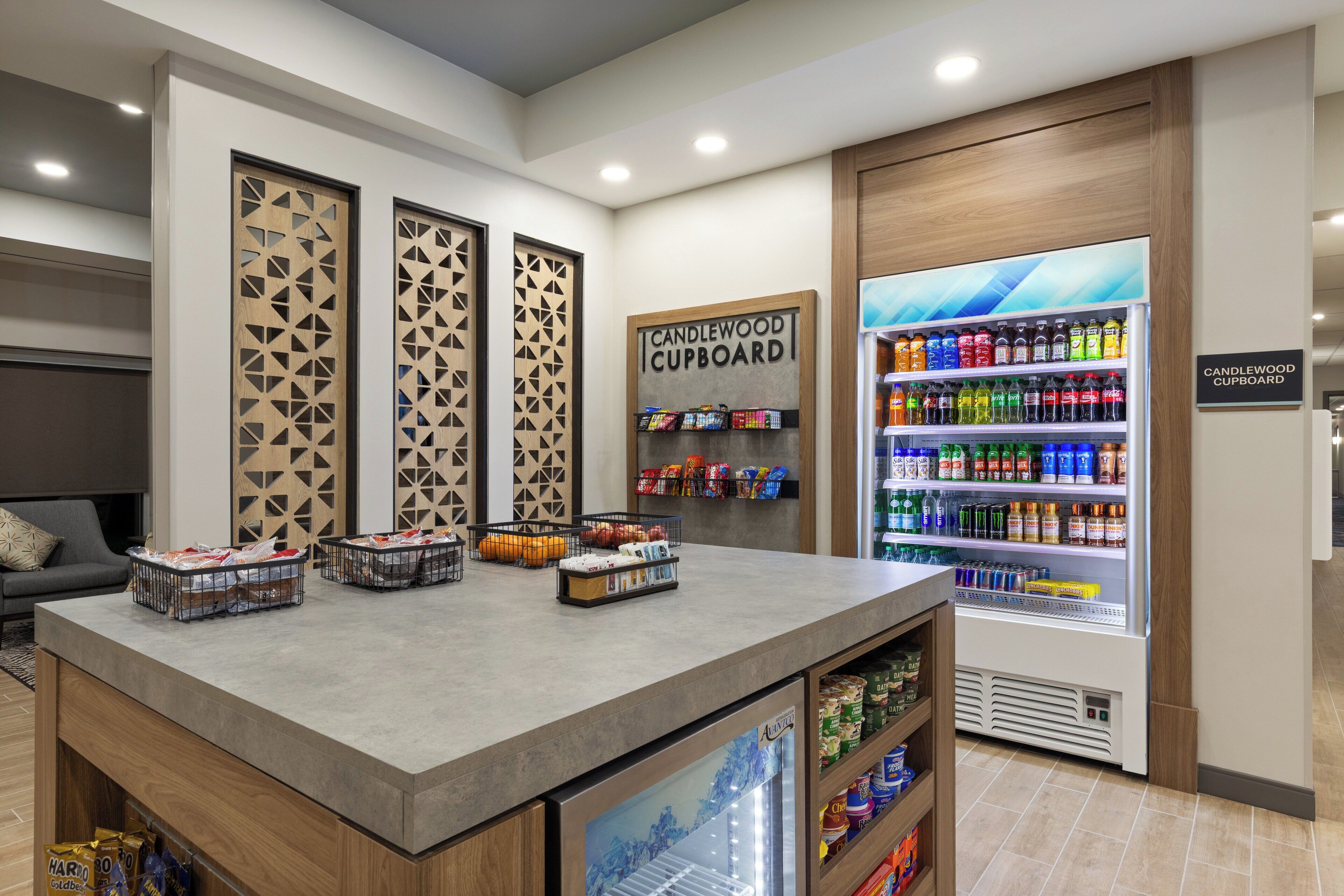 A self-service area with a refrigerated beverage dispenser, snack bins, and a sign for the Candlewood Cupboard.